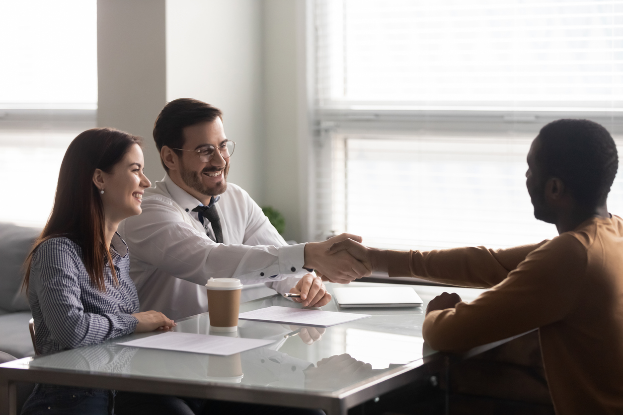 Happy recruiter handshake greeting with african American male work candidate at interview in office, smiling HR manager shake hand of man applicant closing deal thanking for successful talk